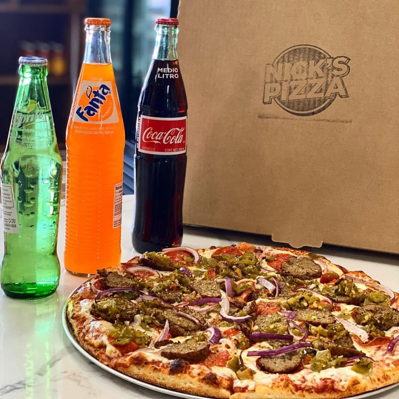 Nick's Pizza with sausage, peppers, and onions, alongside a pizza box and three soda bottles.
