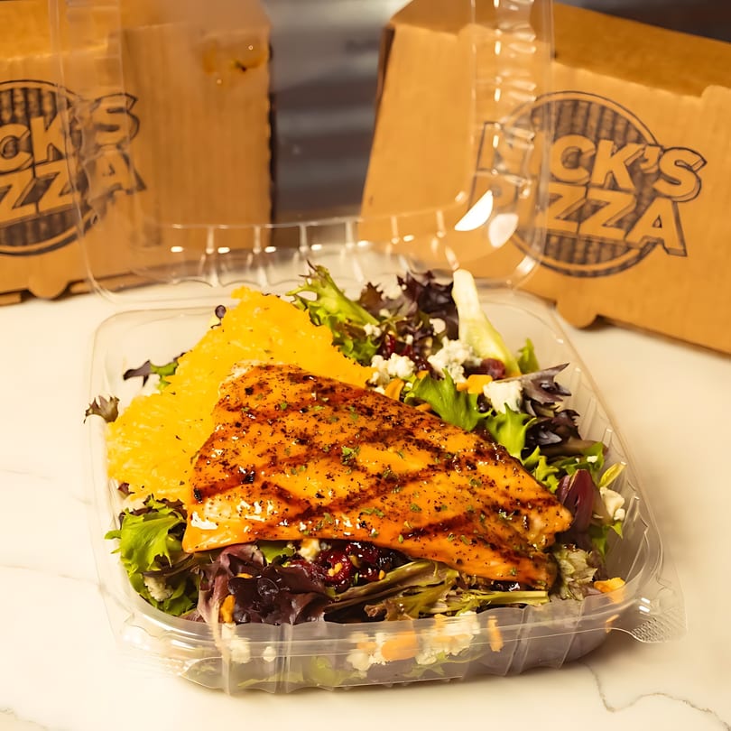 Grilled salmon salad with mixed greens and oranges in a clear plastic container from Nick's Pizza.