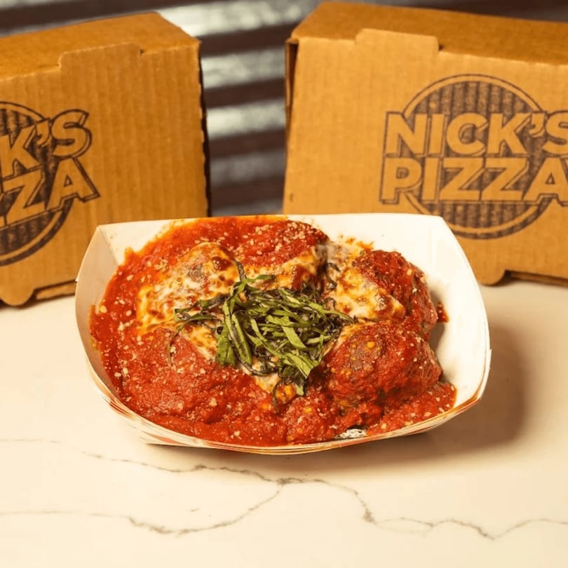 Meatballs in red sauce with melted cheese and basil, with two Nick's Pizza boxes behind.